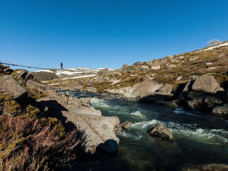 A person walking on a bridge over a stream in the NSW Snowy Mountains