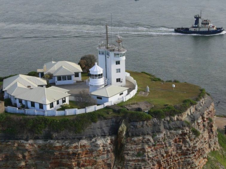 Nobbys Lighthouse close-up. You can see 3 cottages and the lighthouse. A tug boat is sailing past.