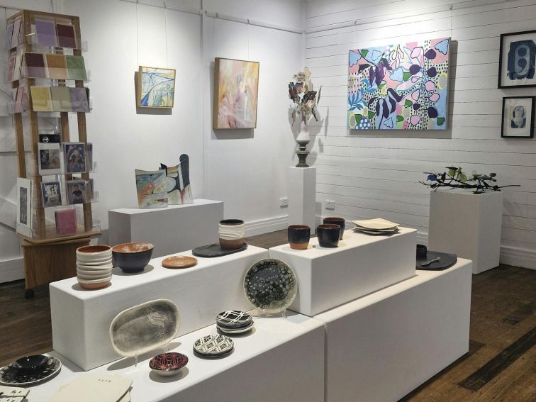 room in gallery with artworks, ceramics, paintings, sculptures and card rack.