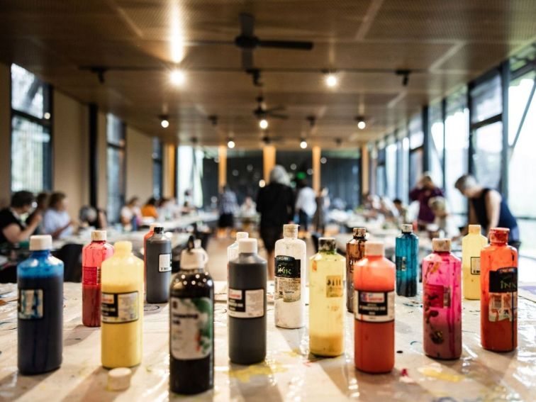 A selection of different coloured paints in the foreground during an adult artmaking workshop