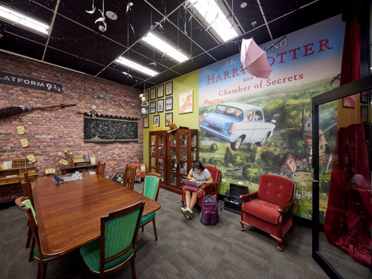 A teenager sits on a lounge chair in a library room decorated in a Harry Potter theme.