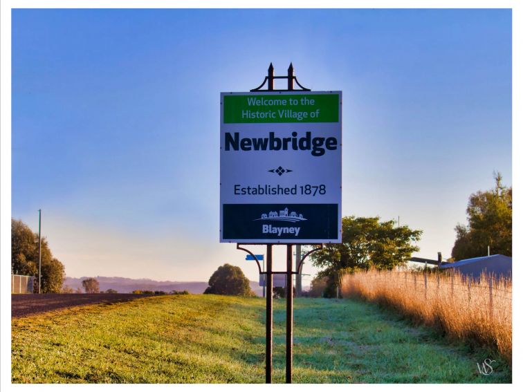 Tricolour road sign on street verge:  Welcome to the historic village of Newbridge est 1878