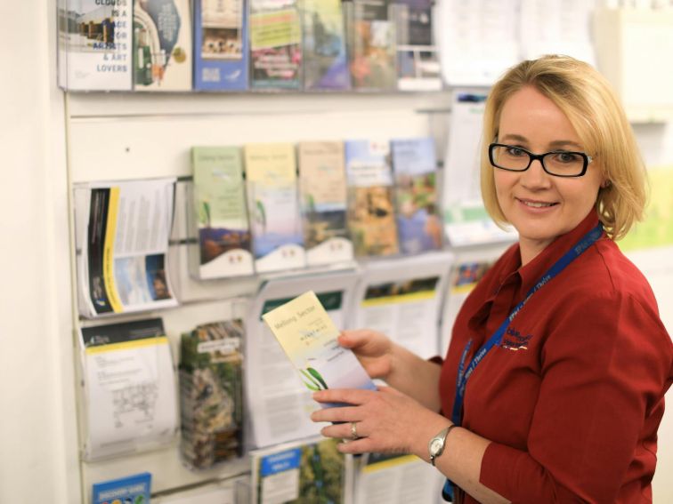 Female staff member standing in front of brochure display ready to assist customers