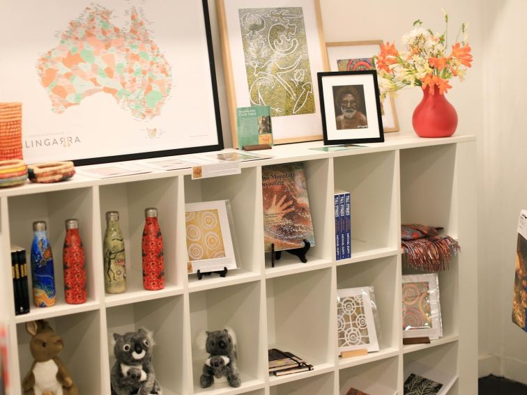 A range of souvenirs  including maps and water bottles displayed on the shelves of a white bookcase.