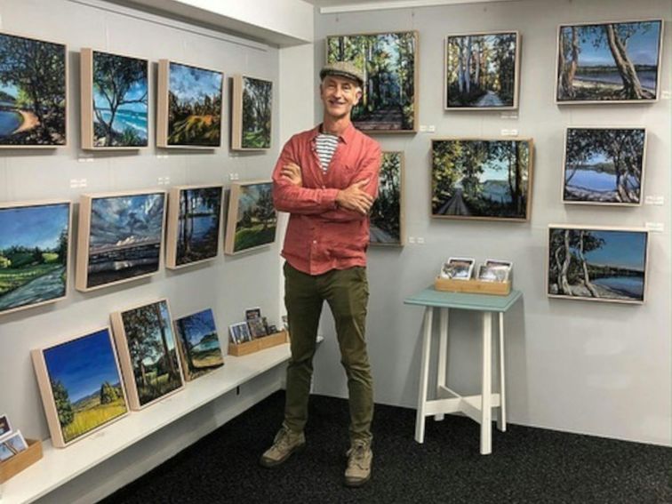 Artist standing in front of walls full of his artworks