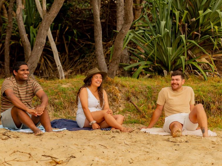 One lady and two men sitting on the beach