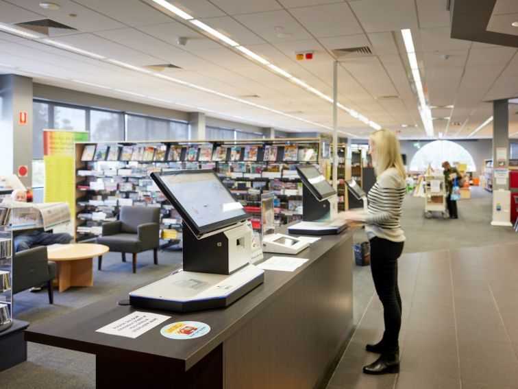 A staff member checking out books using a self-check kiosk.