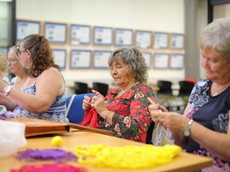 Four women sit happily at a table, knitting and sewing.