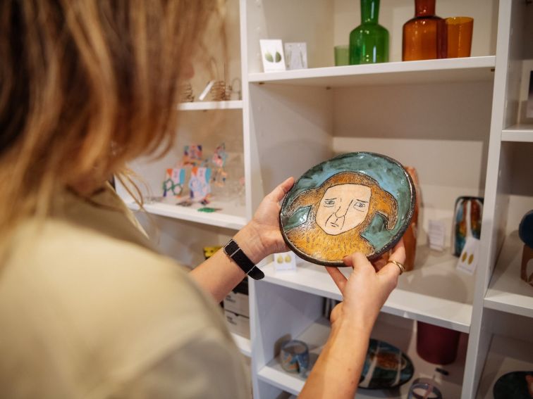 Two hands holding a small plate with a painted face on it