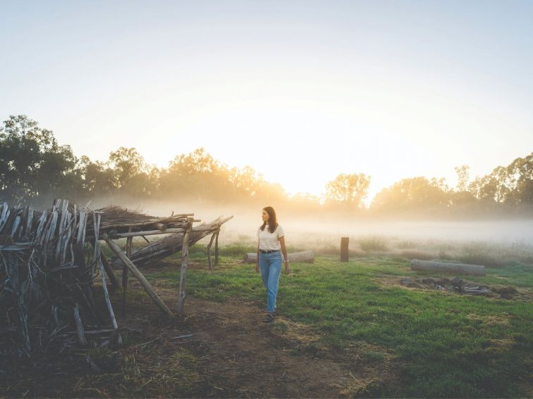 A women walking past structures made from natural material on a foggy morning in a wetland