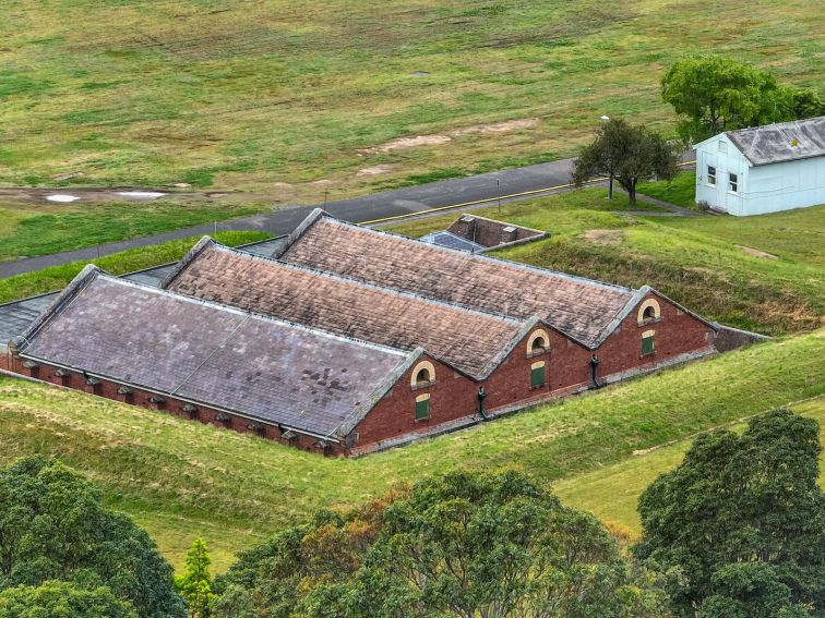 Birds eye, drone view of red brick heritage building with 3 gable roofline, surrounded by grass.