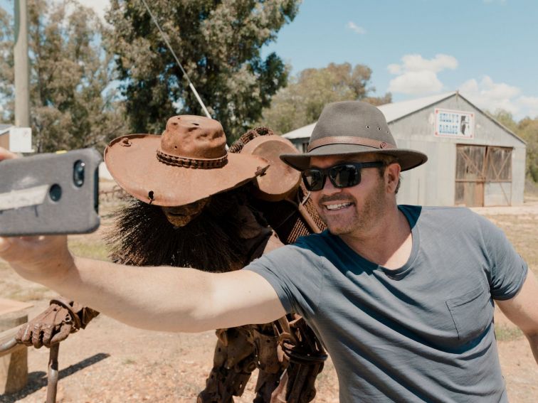 A man takes a selfie with the scrap metal swagman sculpture.