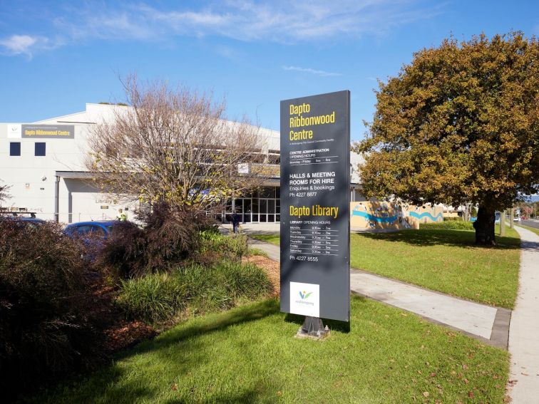 Lawn, large tree and totem signs outside Dapto Library at Ribbonwood Centre