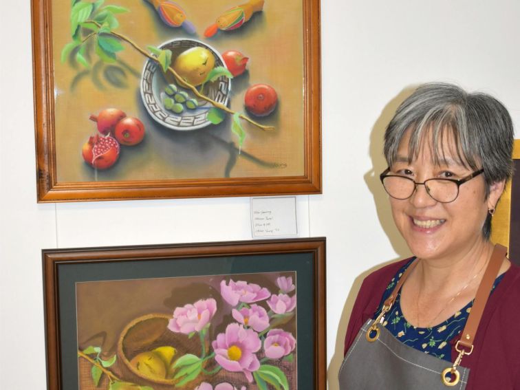 The artist, Young Till, smiling beside her pastle artworks of still life.
