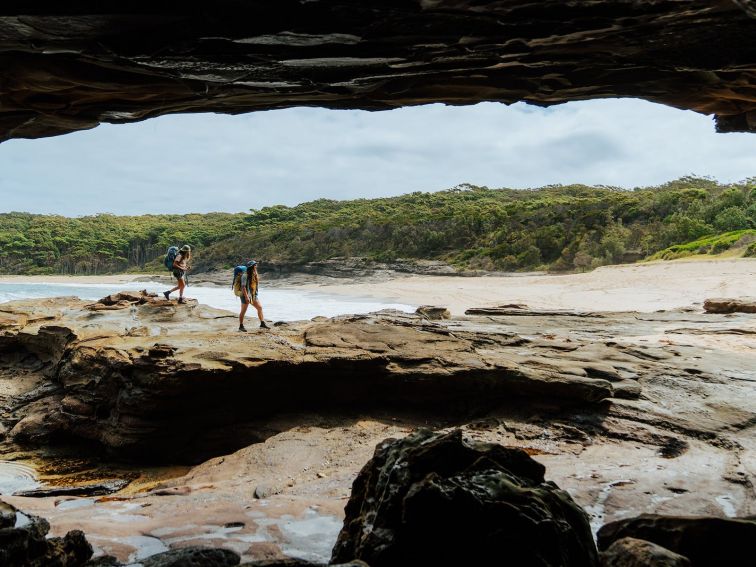 Two people walking over rocks with Emily Miller Beach in the background