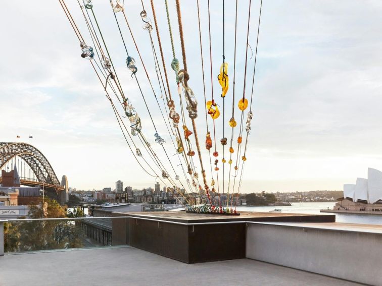 An artwork on a balcony overlooking the Sydney Harbour Bridge and Sydney Opera House.