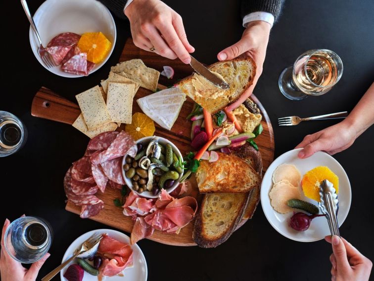 An overhead shot of cafe goers enjoying a selection of cheeses, fruit, charcuterie and vread