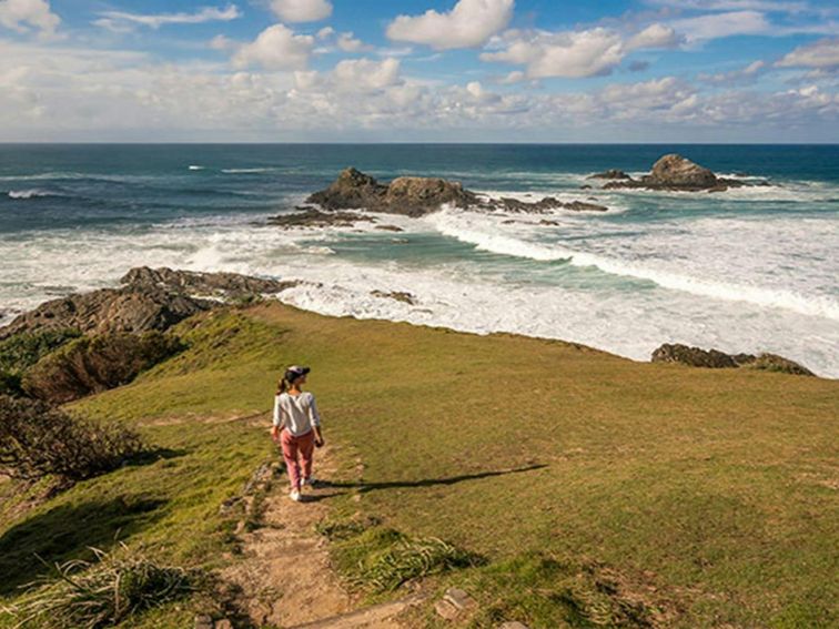 A woman walking down Three Sisters walking track towards the ocean in Broken Head Nature Reserve.