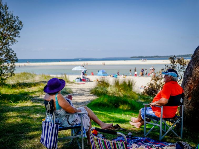 Couple sitting in the shade of a tree looking out to swimmers at Moona Moona Creek