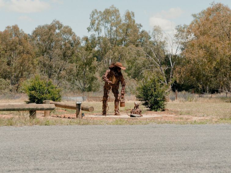 A scrap metal swagman and dog, set in a rural Australian landscape.