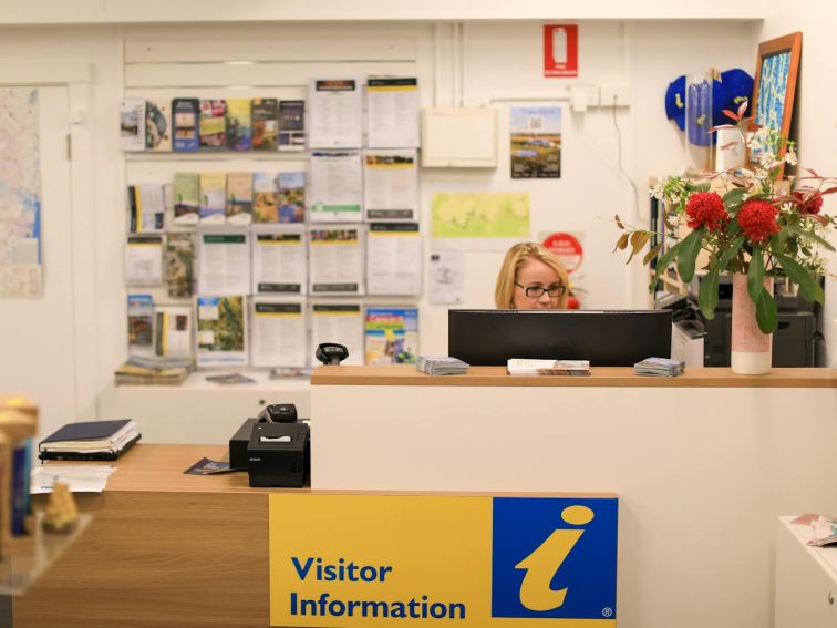 Staff member wearing red uniform sitting behind computer at the information desk working busily