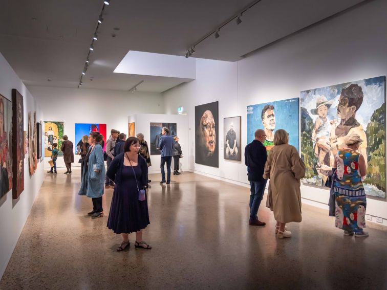 A number of people move through an art gallery with large paintings on the walls