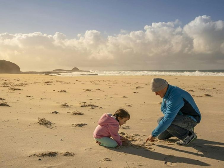 A father and baby daughter playing on the sand at the beach, Haycock Point picnic area, Beowa