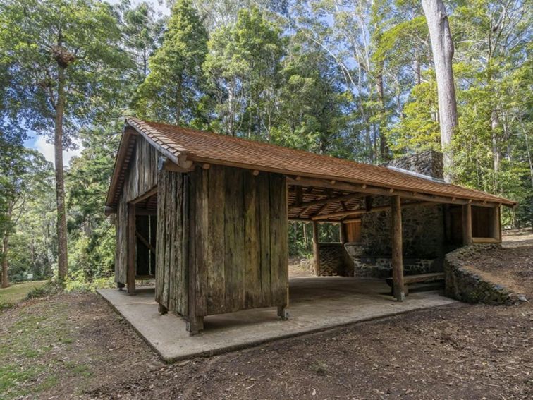 One side of the historic wooden picnic shelter, showing its gabled roof and timber frame at Never