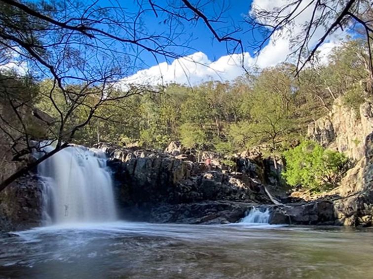 Water cascades over rocky ledges into a pool surrounded by bushland in Horton Falls National Park.