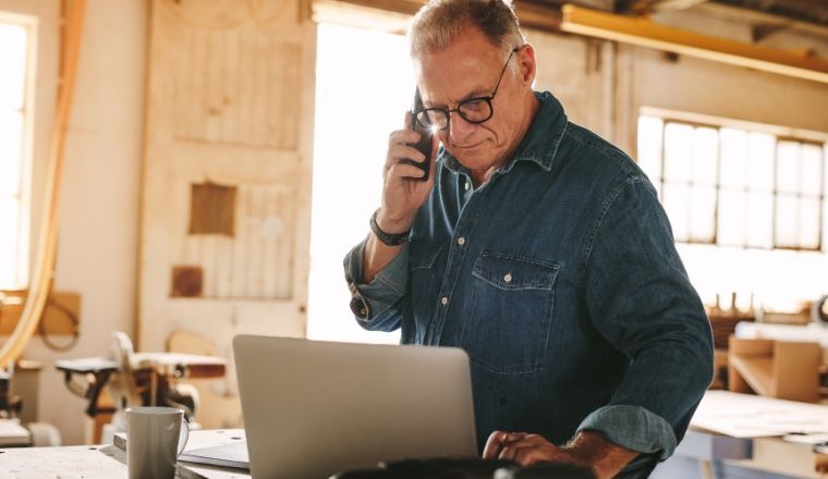 Man talking on a mobile phone using a laptop on a work table