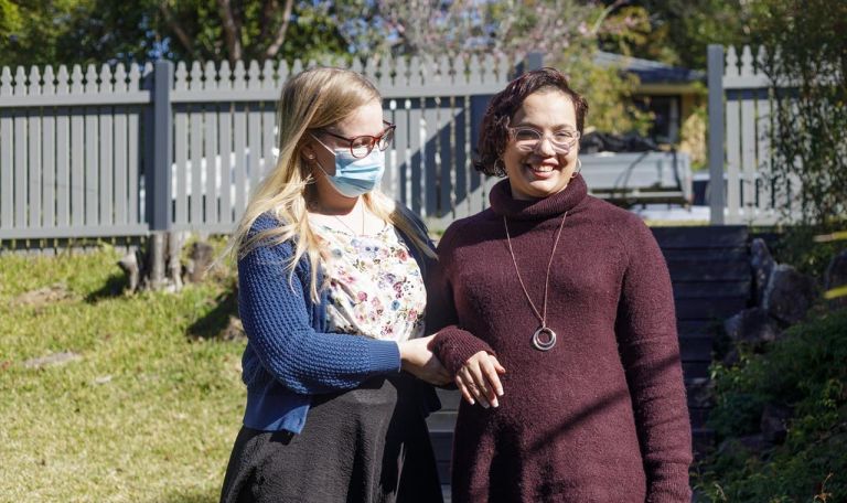 Woman being helped by carer outside a house