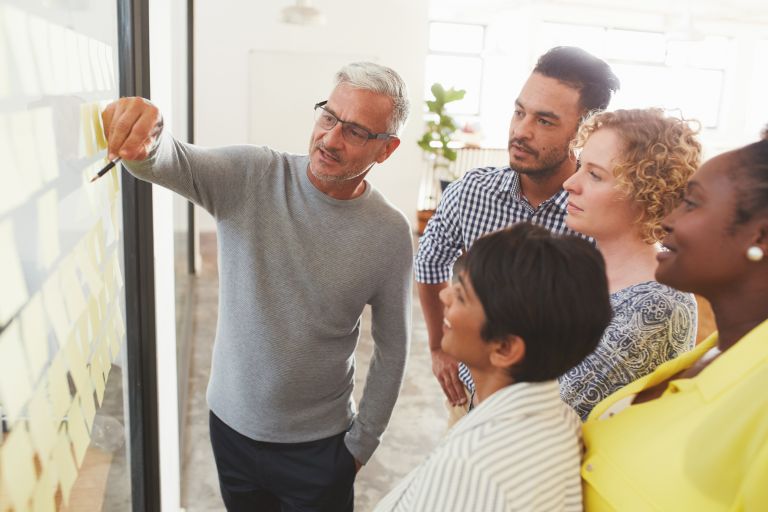 Man pointing to left of image, with group to his right looking in same direction.