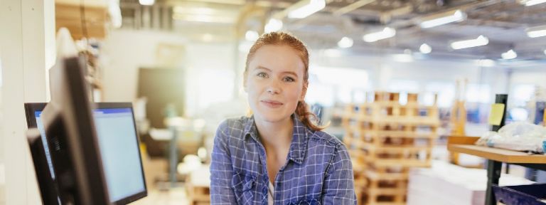 Closer view of young woman in blue shirt seated in front of desktop computer monitor.