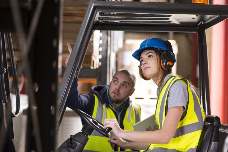 Man advising female forklift driver in a safety helmet 