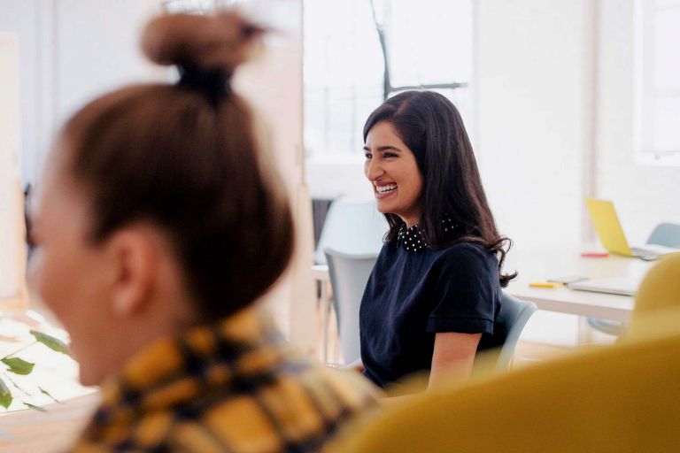 Woman smiling at a conference table in an office, seated next to another woman