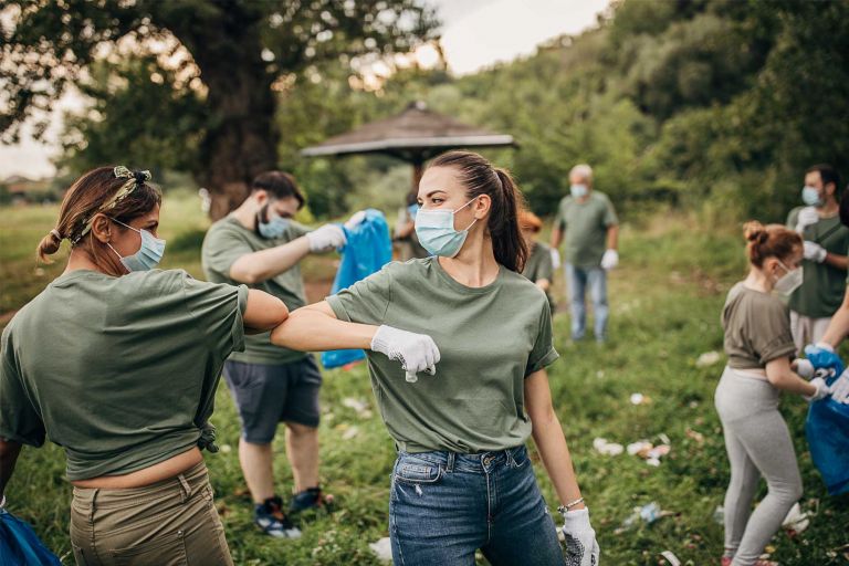 A group collects rubbish in parklands as two women in face masks bump elbows