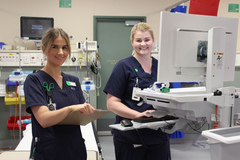 Far West Local Health District nurses smiling at camera while at a computer and equipment station