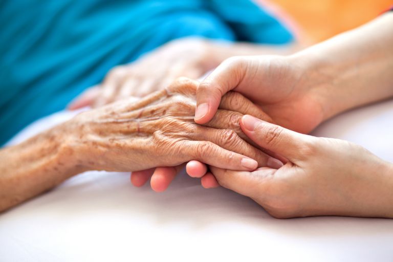 Woman holding senior woman's hand on bed