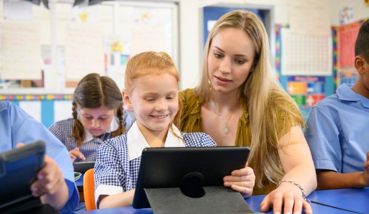 A teacher helping a young girl using a digital tablet in the classroom.