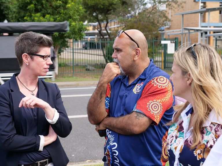 3 adults talking to one another facing away from the camera.