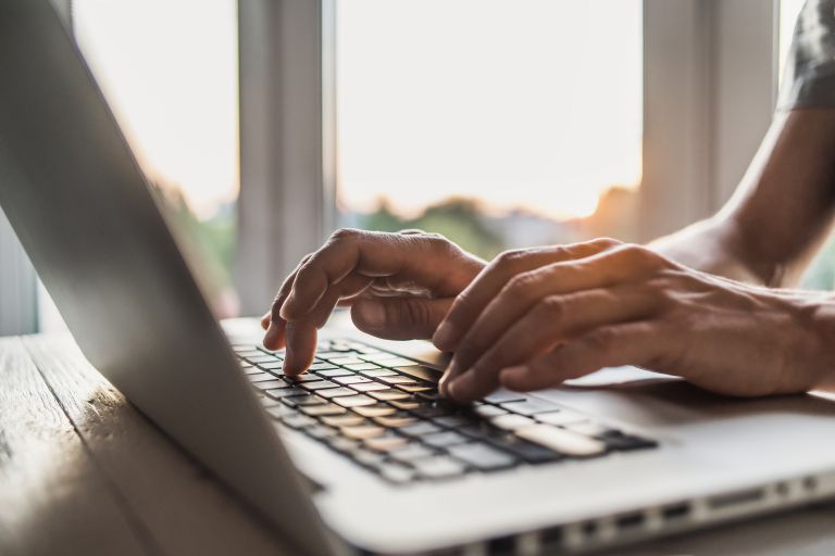 A man typing on his laptop near a window