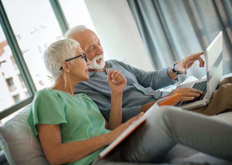 Older couple sitting on the lounge with a laptop computer doing their strata annual reporting tasks.