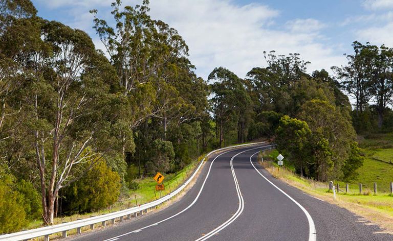 A road with markings and double white line winding through rural landscape with trees either side