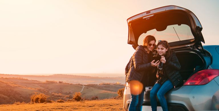 Two people sitting in the boot of a car looking at a phone