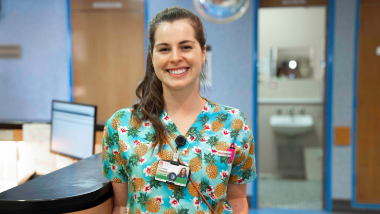 Smiling woman wearing bright shirt with pineapple pattern on, stands in hospital 