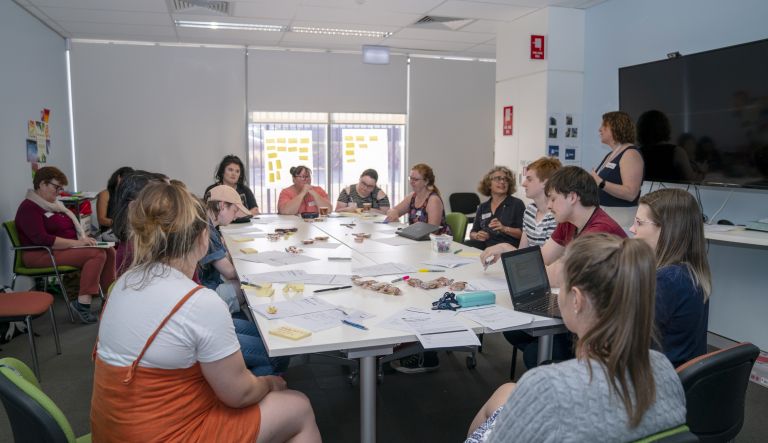 A group of adults sit around a table with papers and biscuits talking to one another