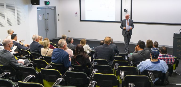 Presenter speaking in front of people in auditorium 