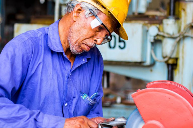 A man in a blue shirt wearing a hard hat and safety glasses uses machiner