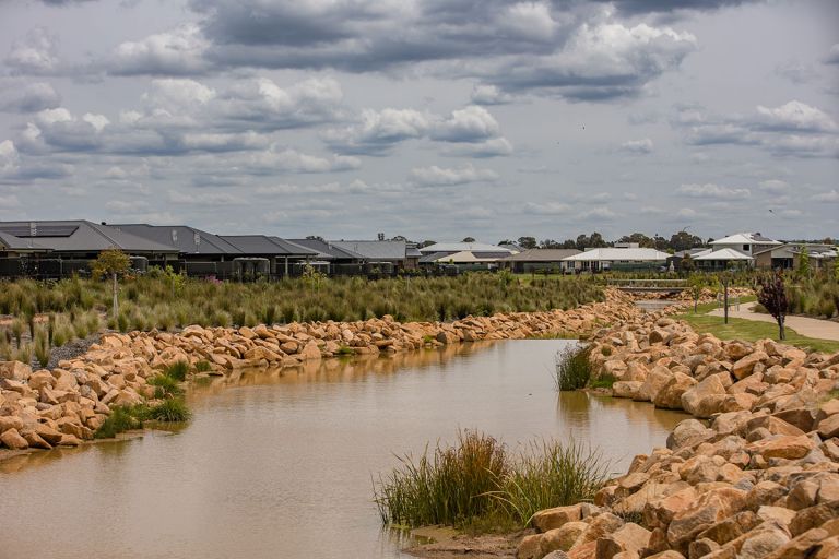 a muddy river winds between sandstone rocks. There are single storey homes on either side of the river