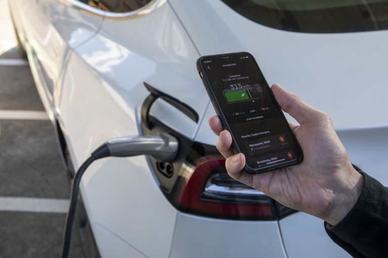 Image of a person holding a mobile while they charge their electric car